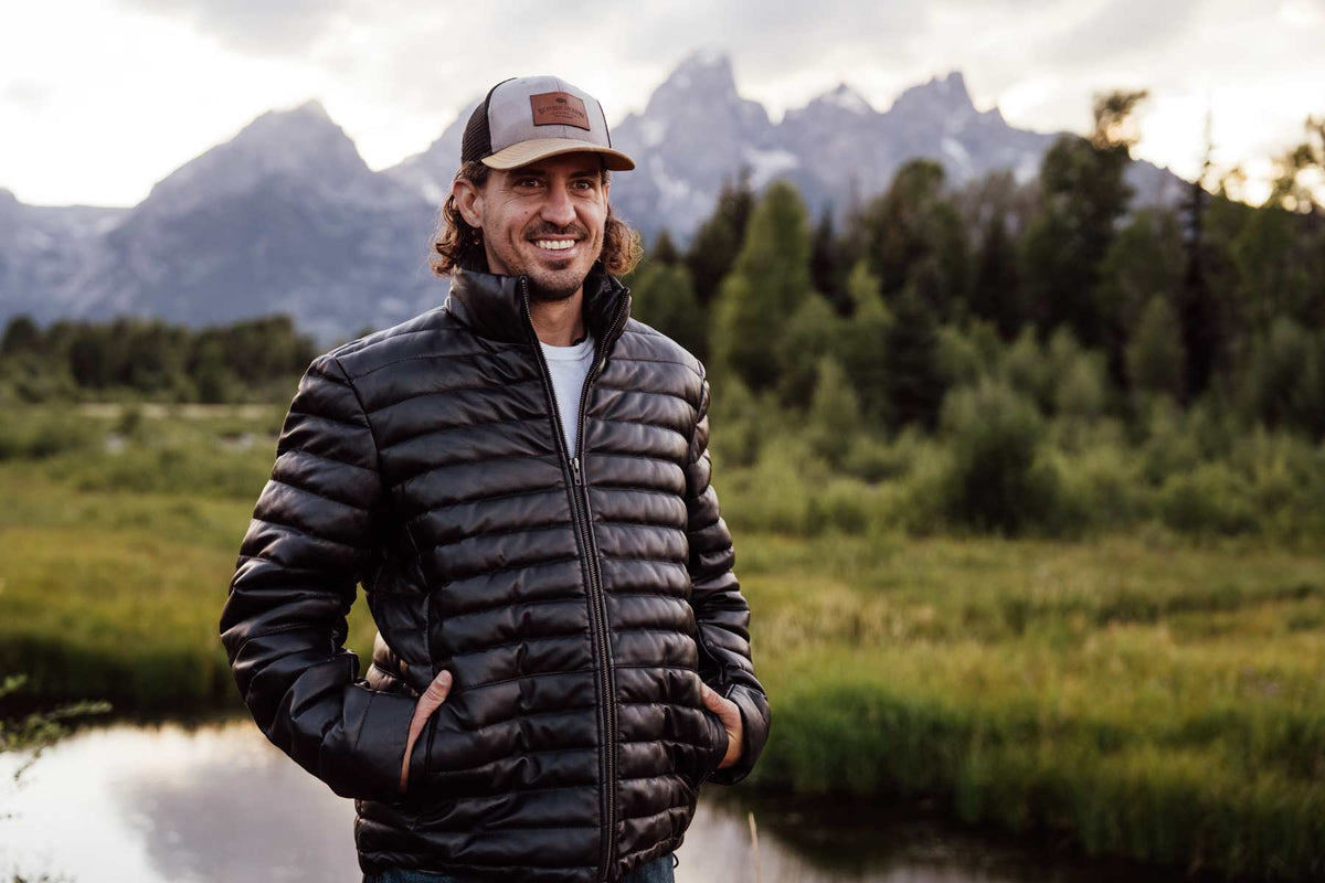 Man wearing the Bridger Leather Down Jacket in Black outdoors in the mountains