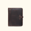Vintage-style dark oak leather travel padfolio with strap and buckle closure, alongside travel essentials.