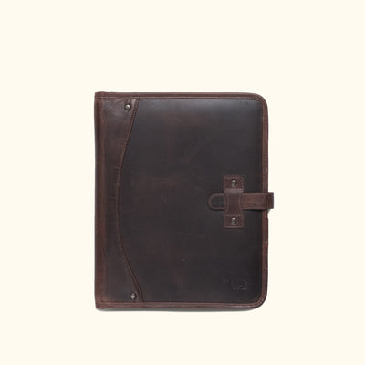 Vintage-style dark oak leather travel padfolio with strap and buckle closure, alongside travel essentials.