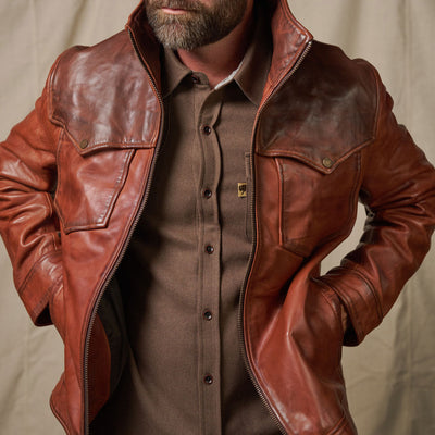 Man wearing a brown leather jacket over a button-up shirt against a neutral background