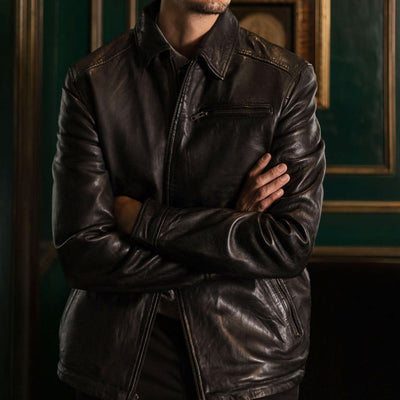 Man wearing a dark leather jacket in a room with green walls and framed pictures.