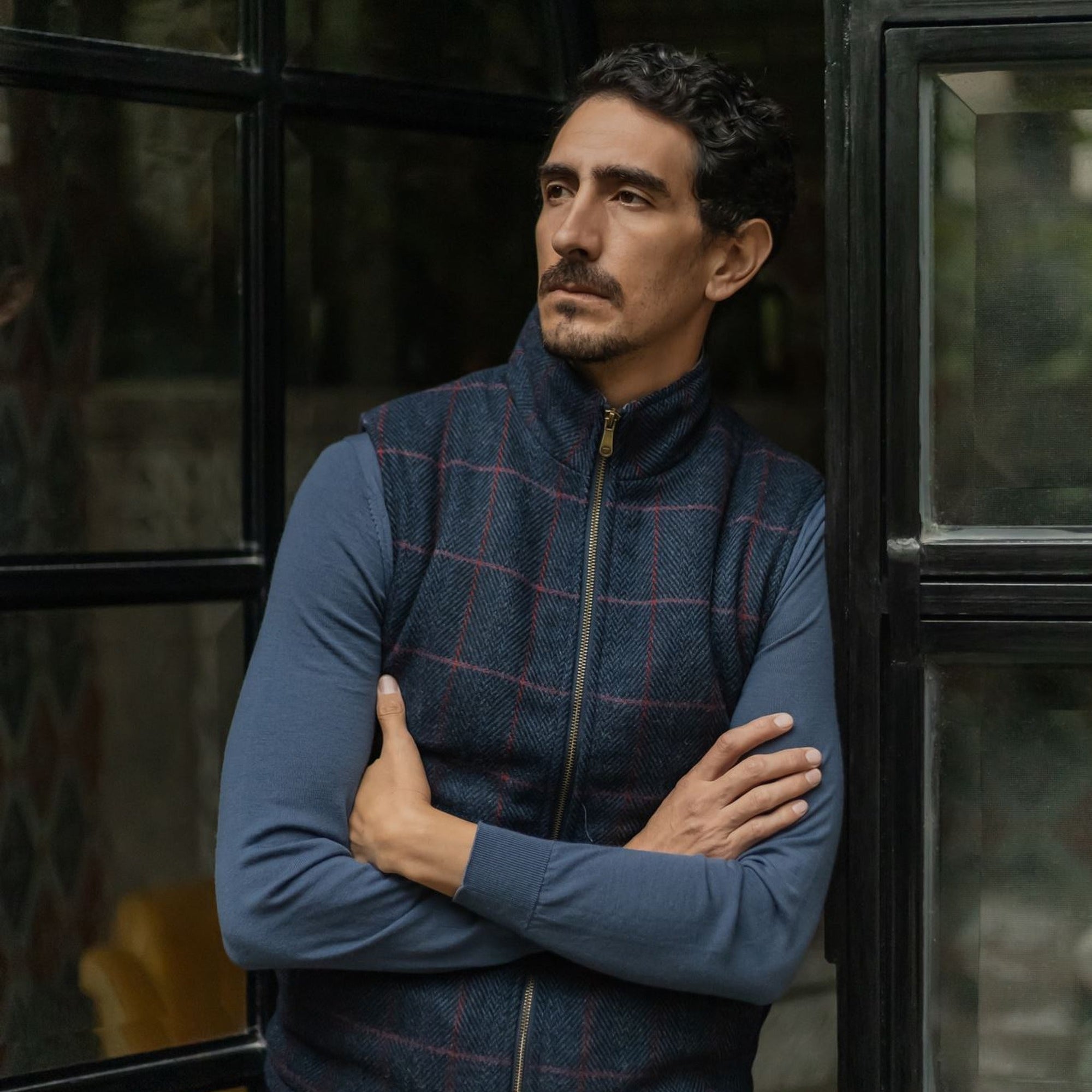 Man in the Ashton Wool Herringbone Vest in Clan Blue with arms crossed by a steel window