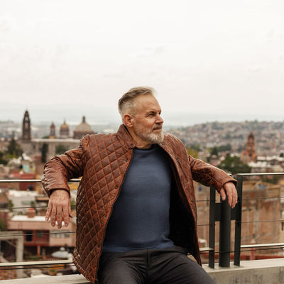 Man in a brown quilted jacket sitting on a rooftop with a cityscape in the background