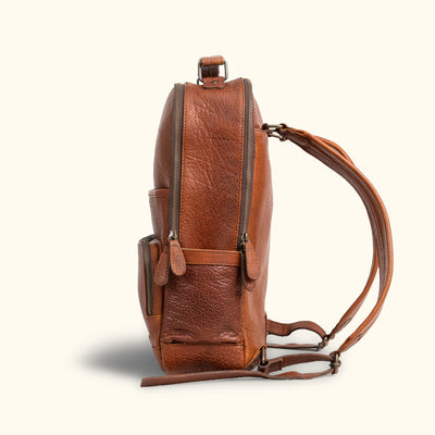 Side View - Rugged brown leather backpack viewed from the side, featuring zipper compartments and adjustable shoulder straps for comfortable carrying.
