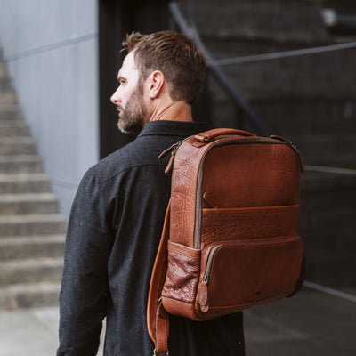 Man in a dark coat carrying a stylish brown leather backpack, walking in an urban environment with a modern design.