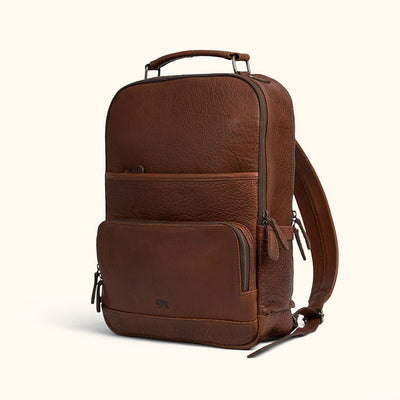 A brown full grain leather backpack with multiple compartments and a cushioned shoulder strap pad