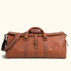 Classic caramel brown leather duffle bag with top handles, detachable shoulder strap, buckle fastenings, and side zipper pocket