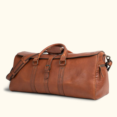 Antique-style caramel brown leather duffle, perfect for travel with its classic design, functional straps, and outdoor-ready construction