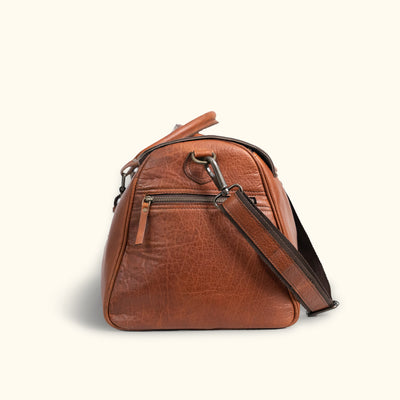 Time-worn look leather duffle bag, with outside pockets, equipped with practical handles and a shoulder strap, suited for adventurous travel and outdoor use.