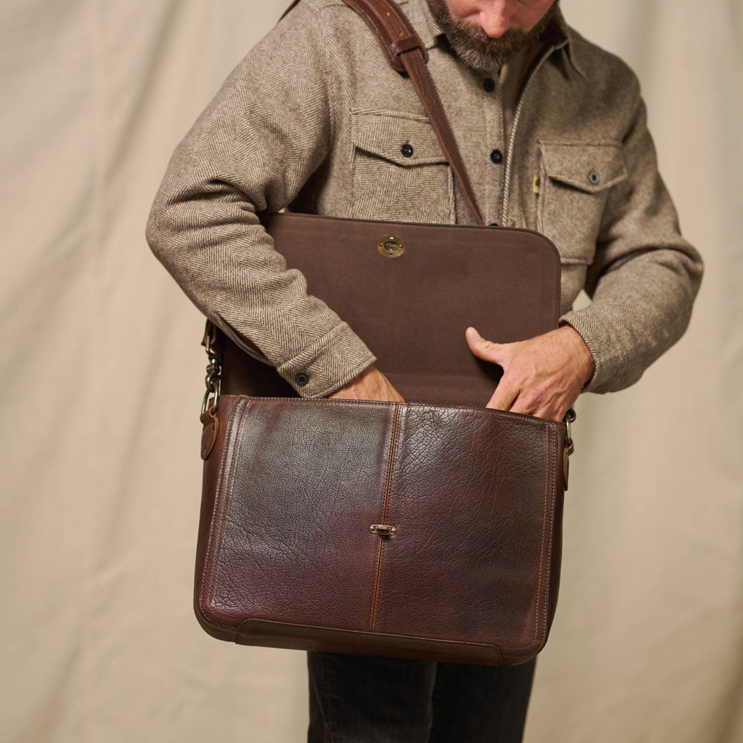 Man holding a brown leather briefcase against a beige background