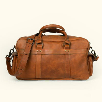Durable amber brown leather pilot bag by Roosevelt featuring robust handles, spacious compartments, and a cross-body strap.