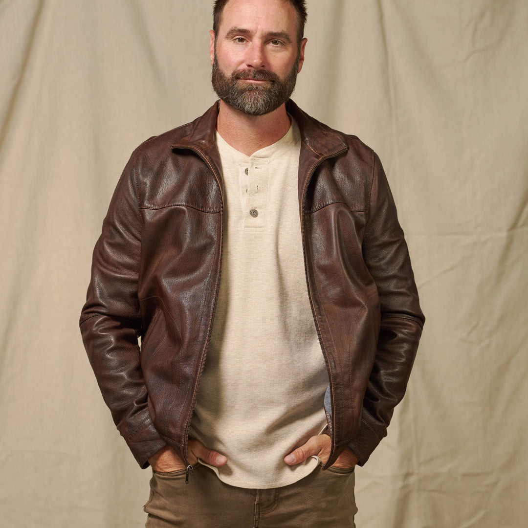 Man wearing a brown leather jacket over a white shirt on a beige background