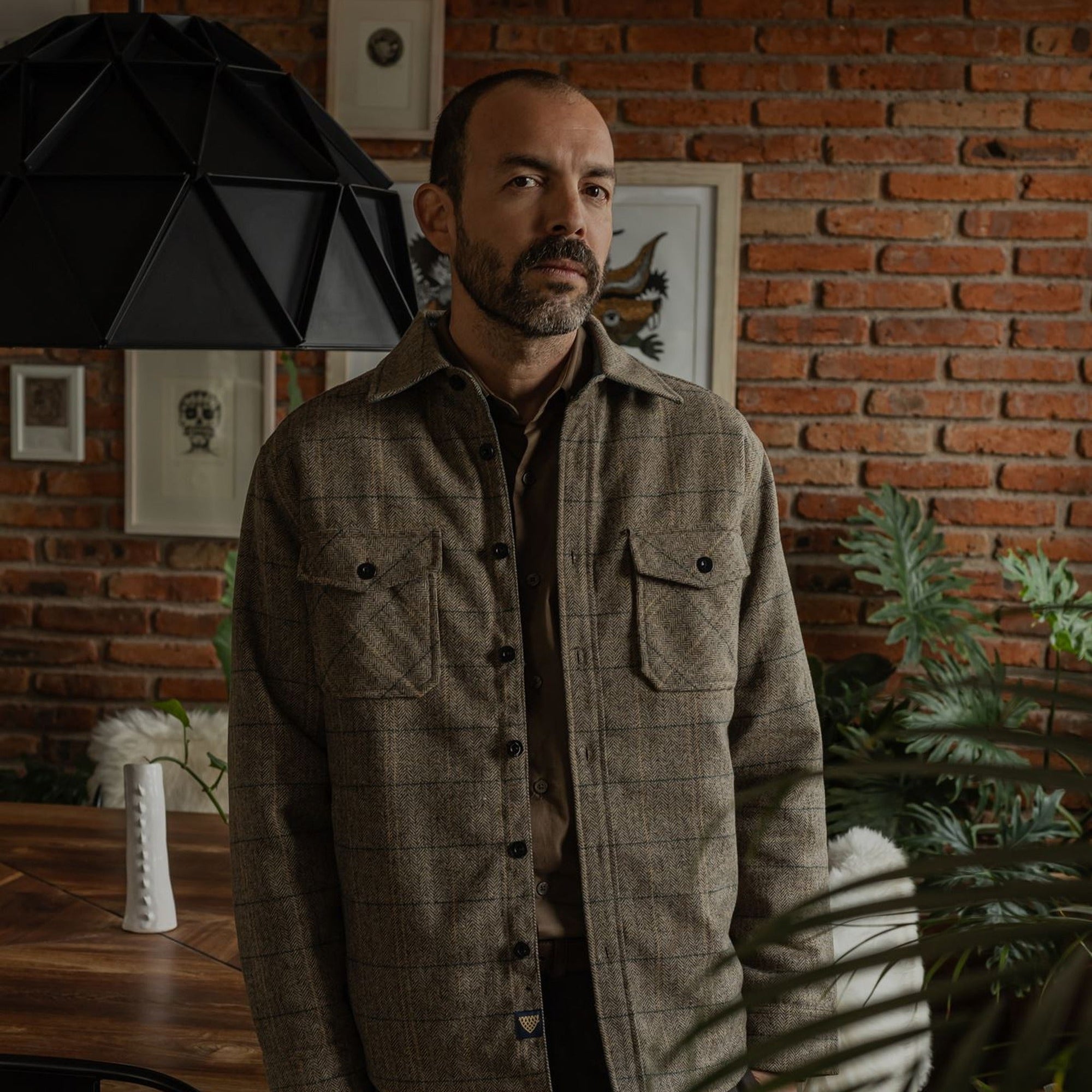 Man in the Aberdeen Wool Twill Shirt Jac in Thistle Grove standing by a brick wall and plants
