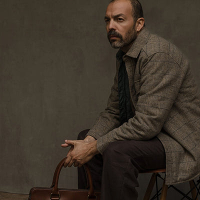 Man in the Aberdeen Wool Twill Shirt Jac in Thistle Grove seated on a stool with a leather briefcase