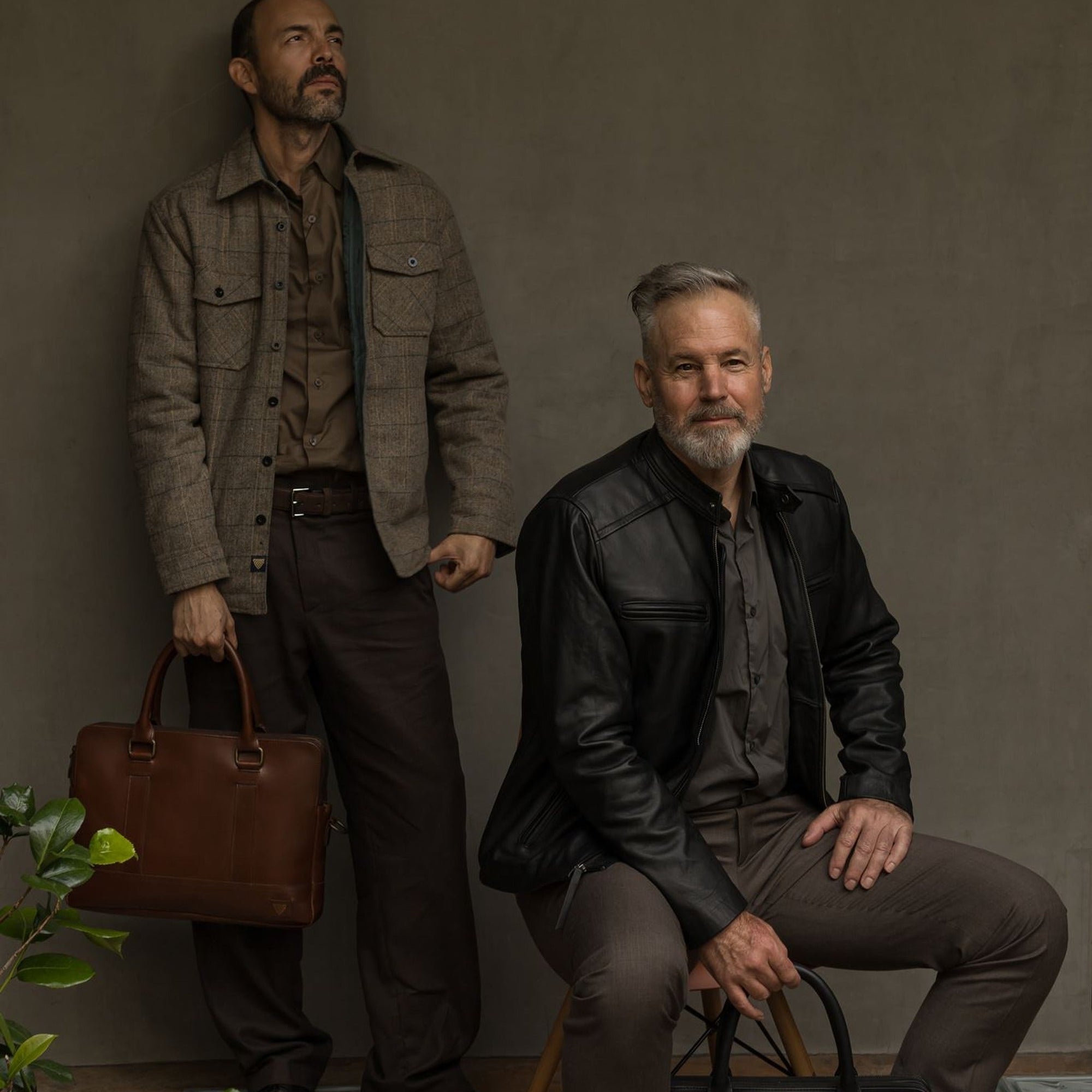 Man in the Aberdeen Wool Twill Shirt Jac in Thistle Grove holding a leather briefcase beside a seated man in a black leather jacket