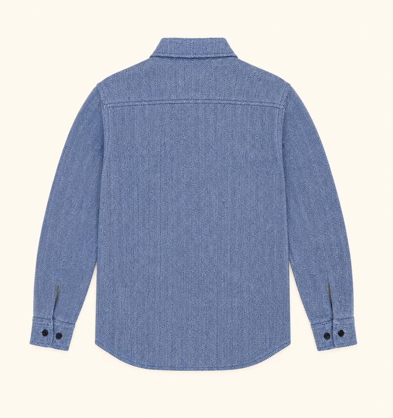 A blue denim long-sleeve button-up shirt shown from the back, laid flat against a light cream background.