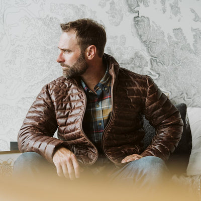 Bearded man in a brown puffer jacket, seated and gazing out the window, exuding a relaxed vibe.