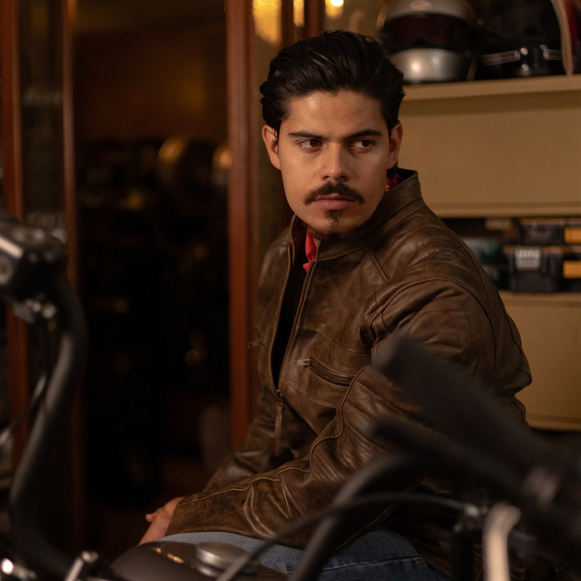 Man in the Cafe Racer Leather Jacket in Distressed Brown seated in a motorcycle garage.