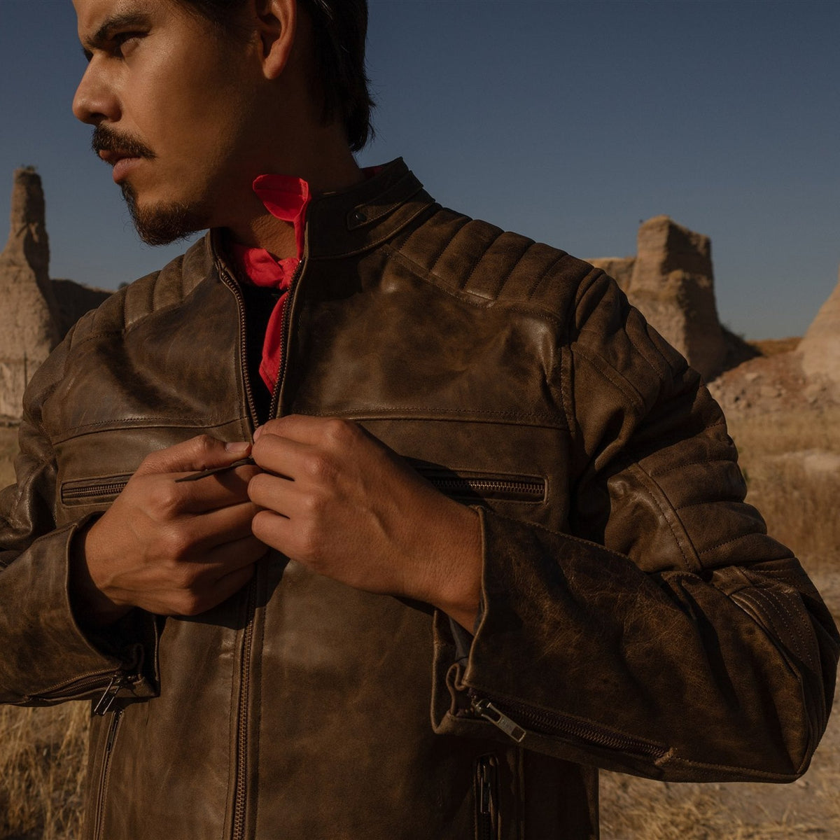 Man fastening the Cafe Racer Leather Jacket in Distressed Brown in dry hills at dusk.