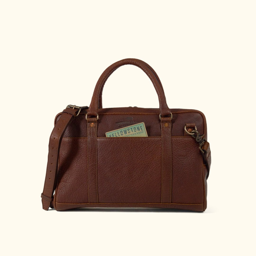 A brown leather laptop briefcase with a brass lock and a shoulder strap, set against a white background.