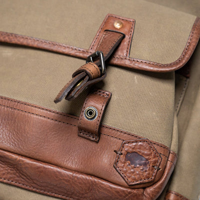 Close-up of a bag's leather buckle and canvas material, showcasing quality stitching and hardware.