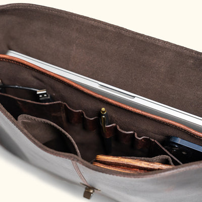 Detailed picture, the inside of a rustic vintage leather bag with a pen, wallet, phone, and computer.