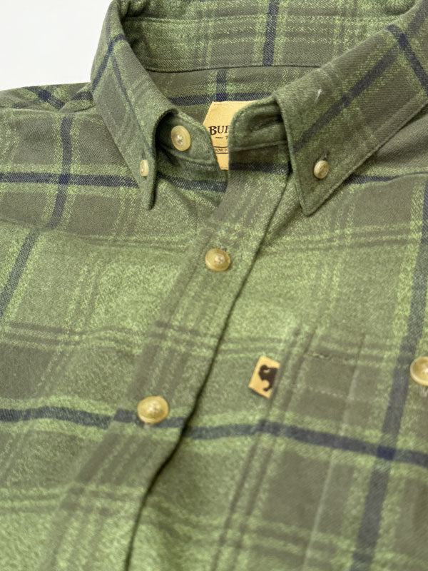 Close-up of a green plaid button-down shirt with brass buttons and a small embroidered logo patch on the chest pocket.