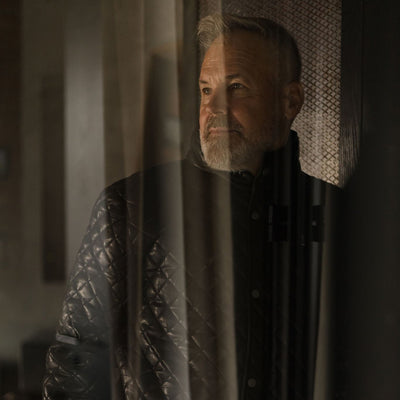 Man in the Highlands Quilted Leather Jacket in Black seen through a sheer curtain.