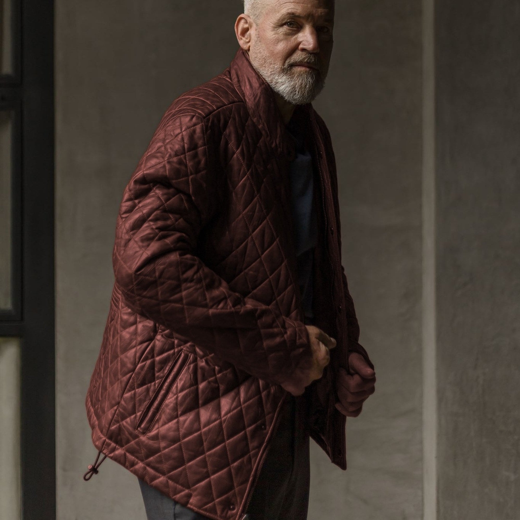Man in the Highlands Quilted Leather Jacket in Mahogany Brown against a concrete wall.