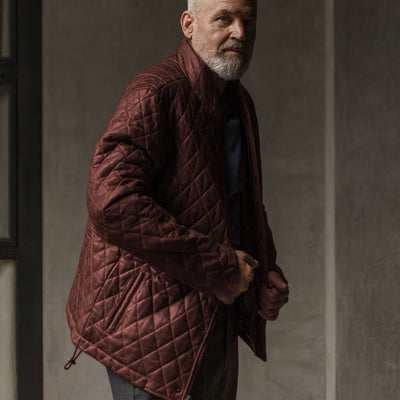 Man in the Highlands Quilted Leather Jacket in Mahogany Brown against a concrete wall.
