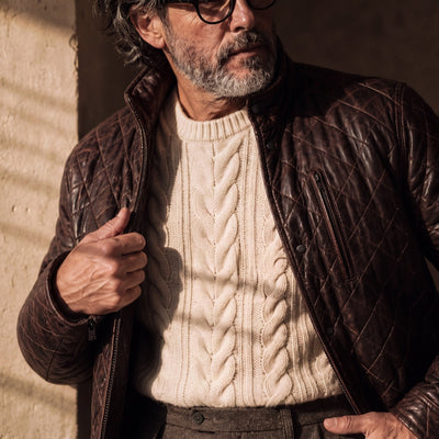 Man in the Highlands Quilted Leather Jacket in Mahogany Brown worn open over a cream cable-knit sweater.