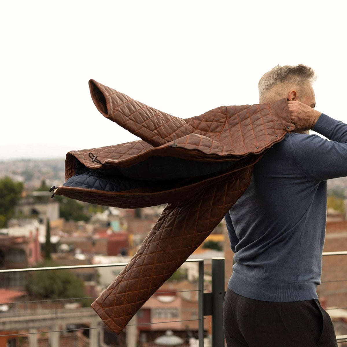 Man swinging the Highlands Quilted Leather Jacket in Whiskey Brown over his shoulder on a city rooftop.