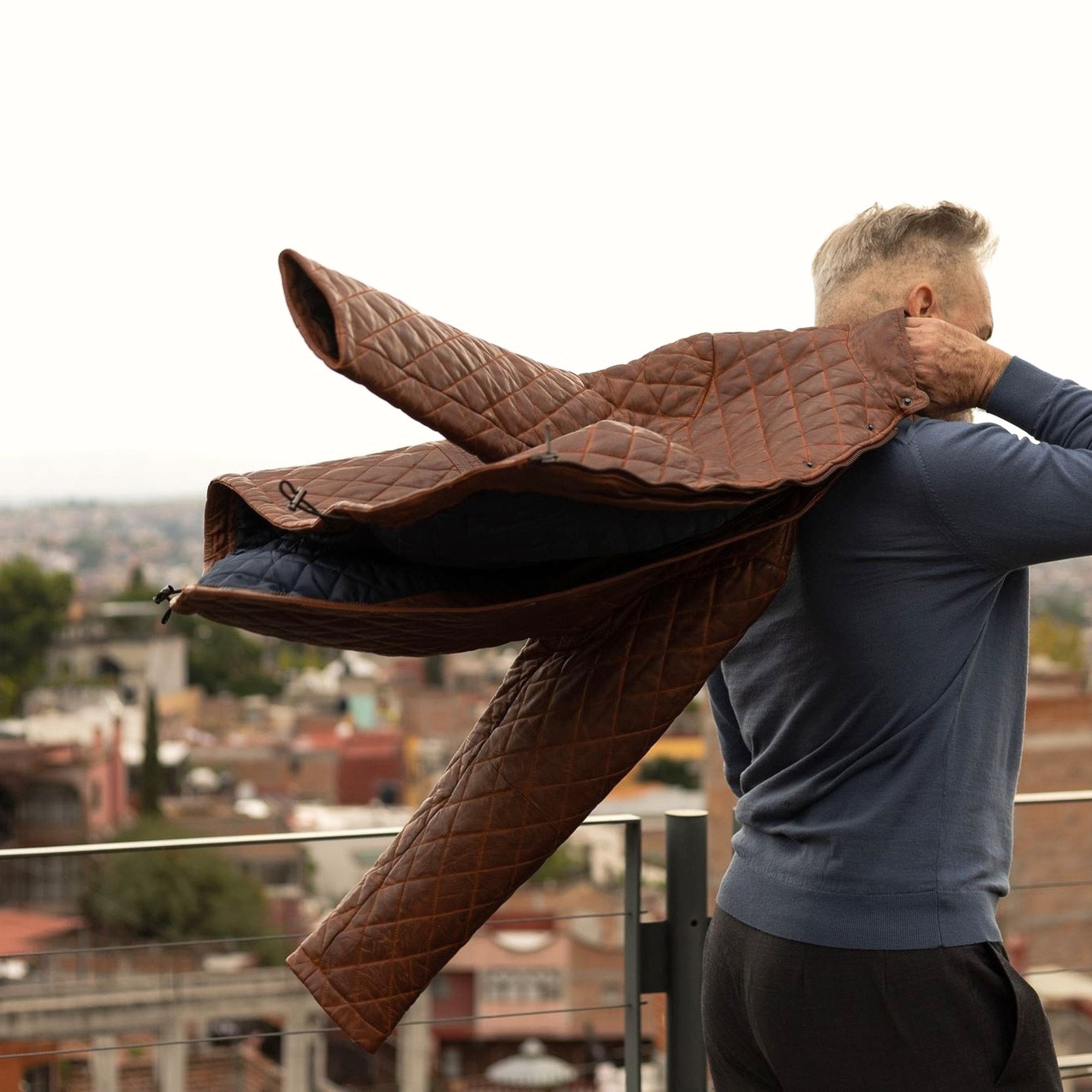 Man swinging the Highlands Quilted Leather Jacket in Whiskey Brown over his shoulder on a city rooftop.