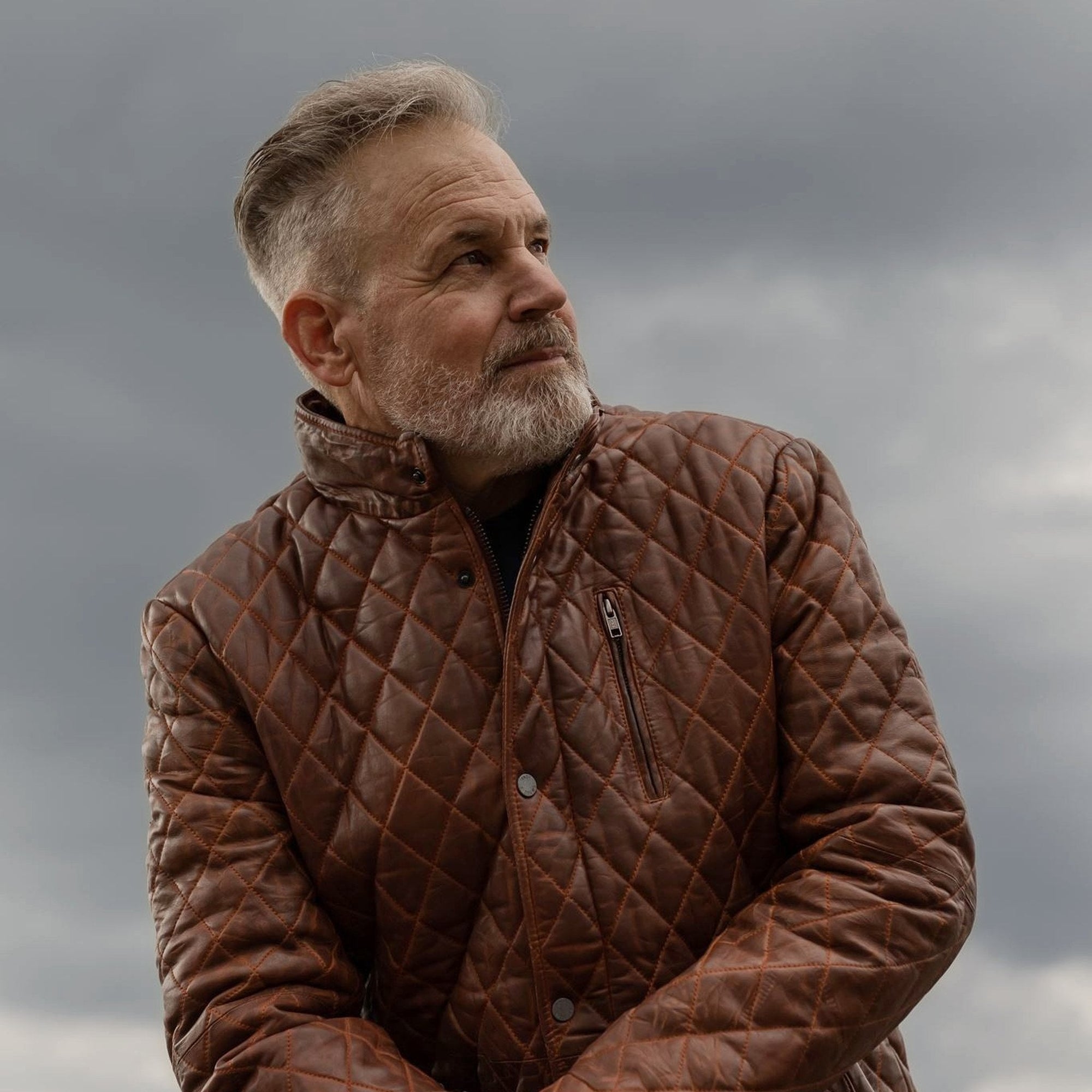 Man seated in the Highlands Quilted Leather Jacket in Whiskey Brown on a rooftop ledge.