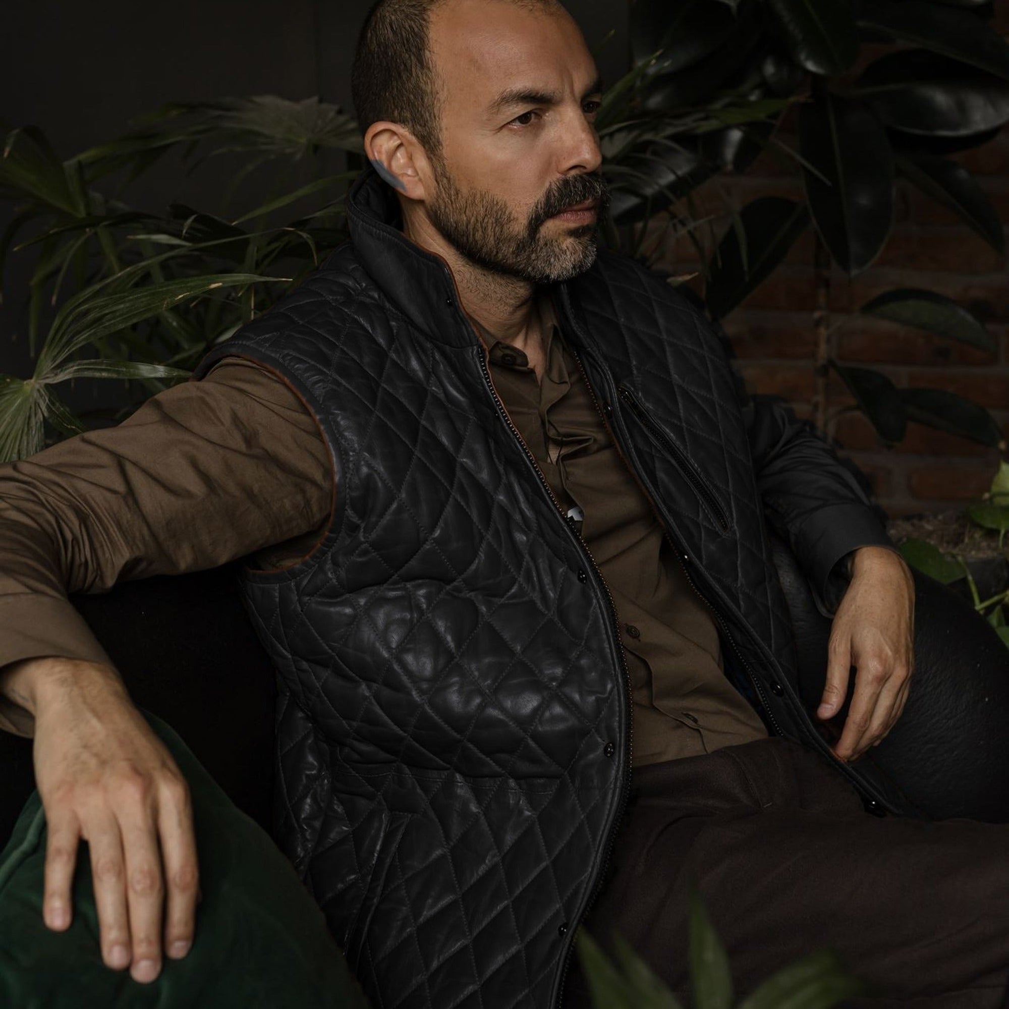 Man seated in an armchair in the Highlands Quilted Leather Vest in Black.