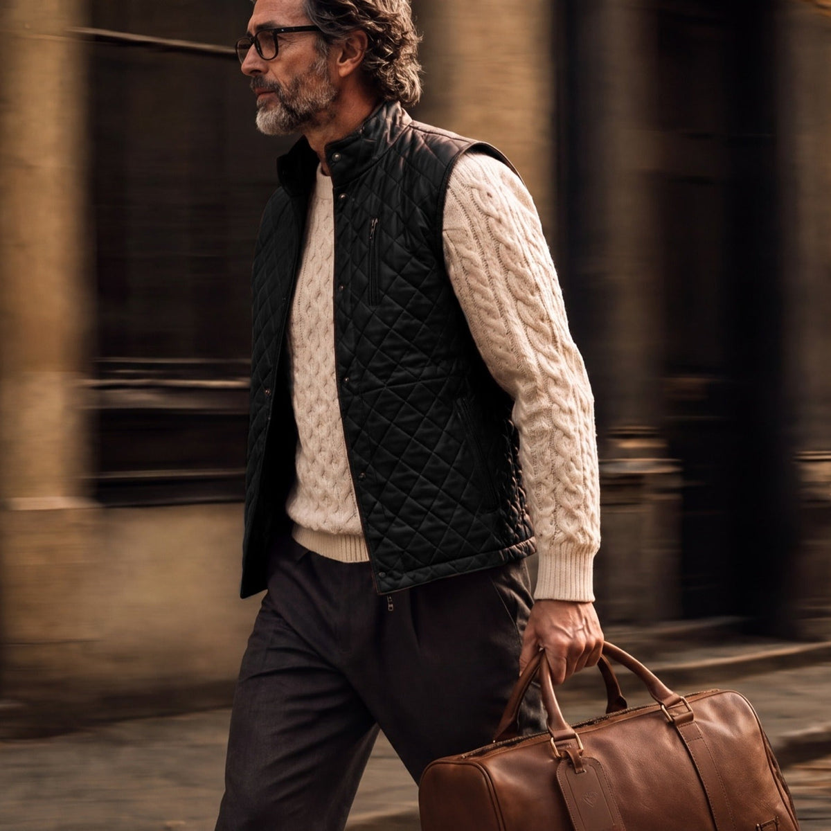 Man walking a cobbled street in the Highlands Quilted Leather Vest in Black with a leather duffle.