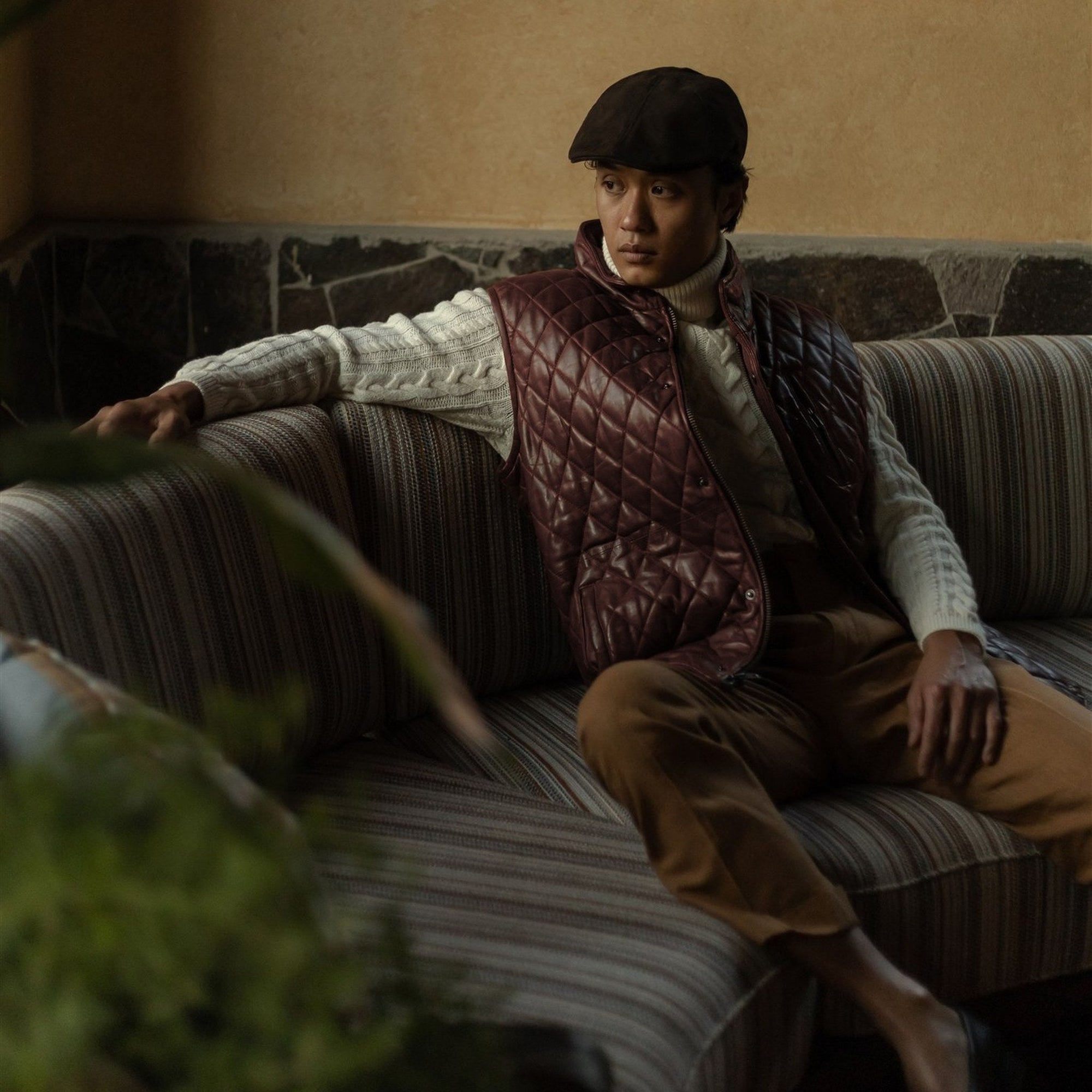 Man seated on a sofa in the Highlands Quilted Leather Vest in Mahogany Brown.
