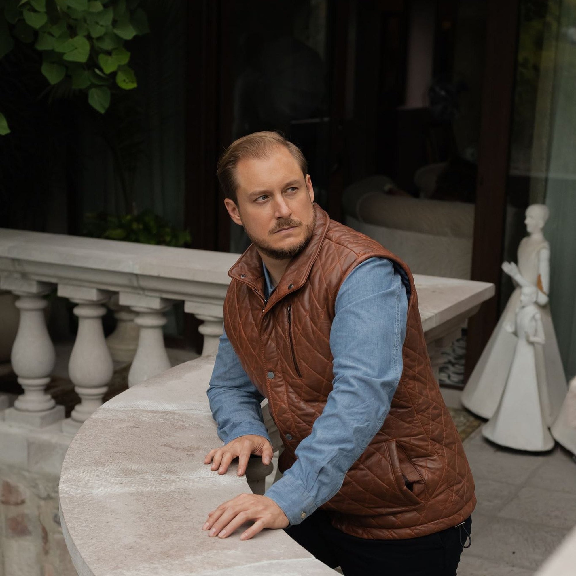Man leaning on a balustrade in the Highlands Quilted Leather Vest in Whiskey Brown.