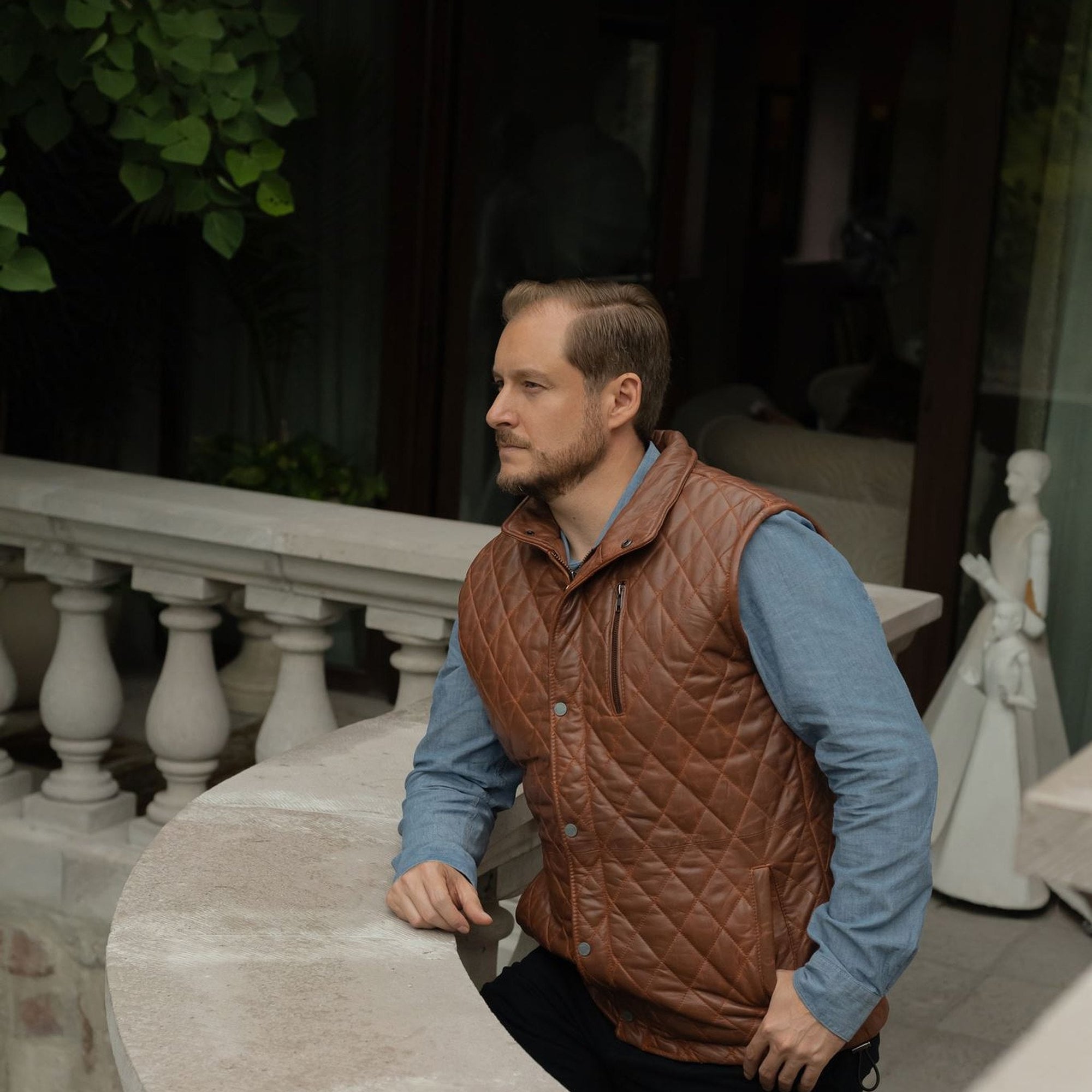 Man on a stone balcony in the Highlands Quilted Leather Vest in Whiskey Brown.