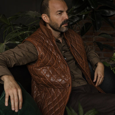 Man seated in an armchair in the Highlands Quilted Leather Vest in Whiskey Brown.