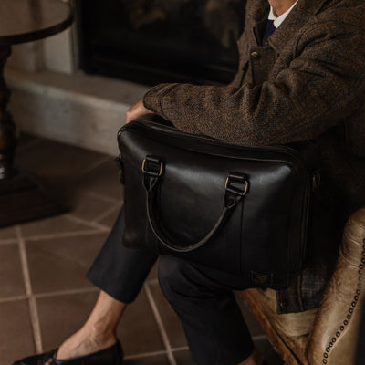 Man seated in an armchair with the Jefferson Leather Briefcase in Vintage Black beside him.