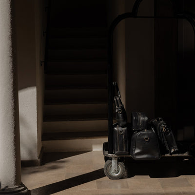 The Jefferson leather collection in Vintage Black on a hotel luggage cart under an arch.