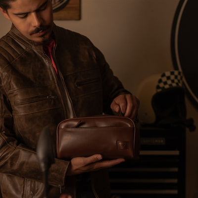 Man in a leather jacket packing the Jefferson Leather Dopp Kit in Elderwood Brown in a motorcycle garage.