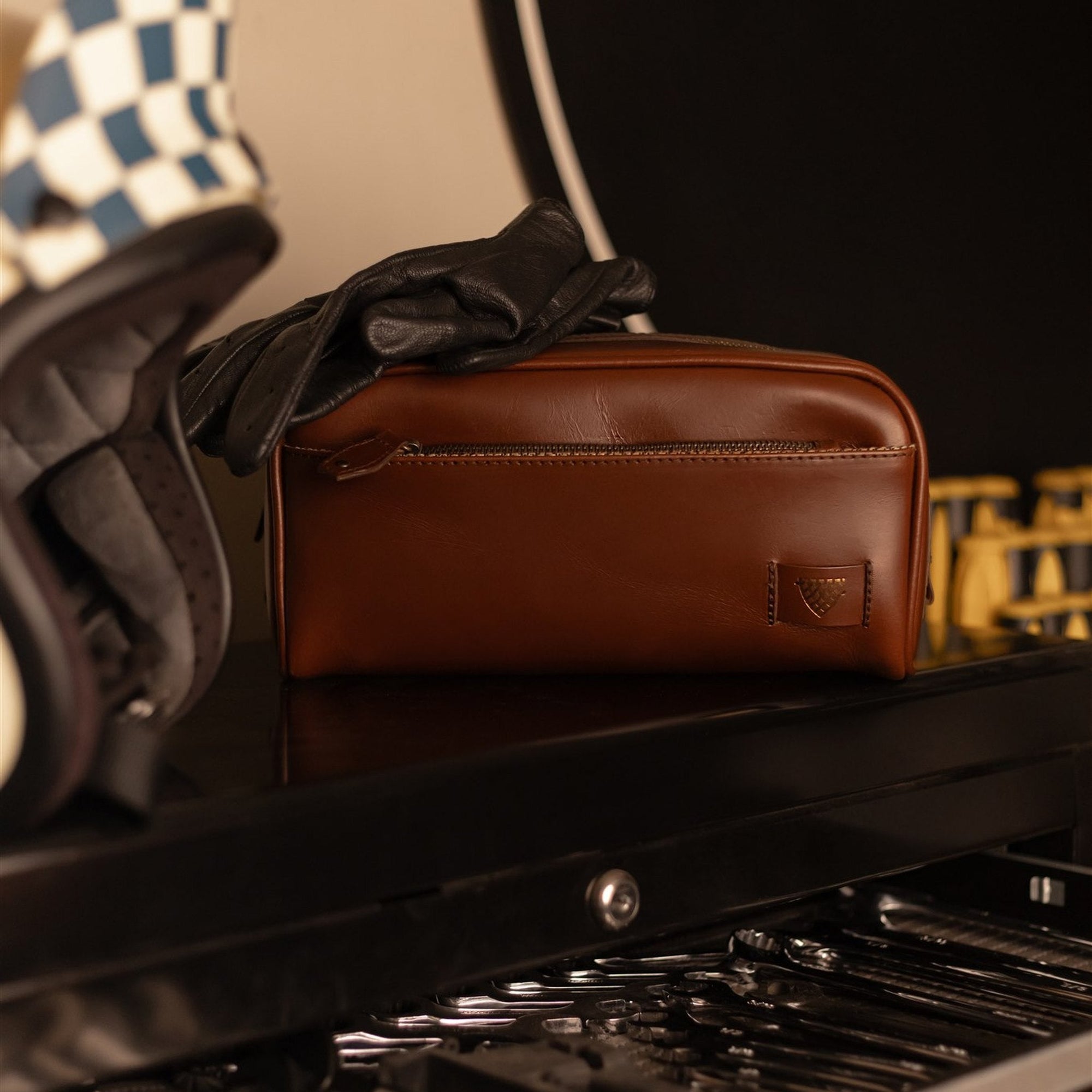 Jefferson Leather Dopp Kit in Elderwood Brown on a toolbox beside motorcycle gloves and a helmet.