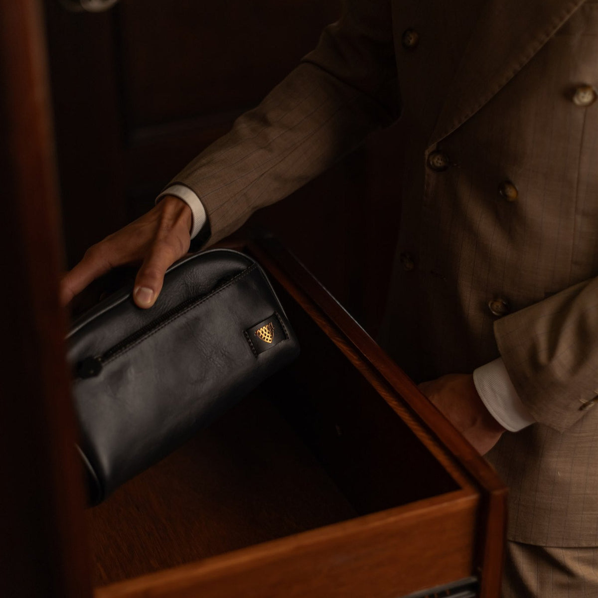 Man placing the Jefferson Leather Dopp Kit in Vintage Black into a dresser drawer.