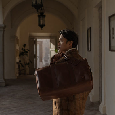 Man holding the Jefferson Leather Duffle in Elderwood Brown in an arched hallway.