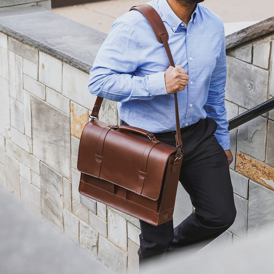 Man holding a brown leather briefcase against a stone wall background