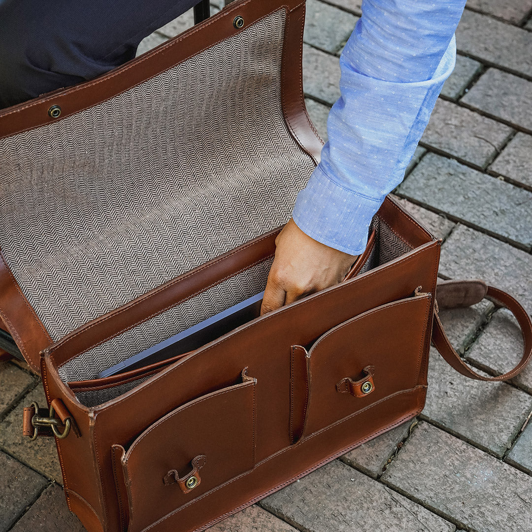Brown leather briefcase with a textured interior, held open by a person wearing a blue shirt.