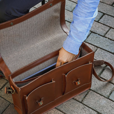 Brown leather briefcase with a textured interior, held open by a person wearing a blue shirt.