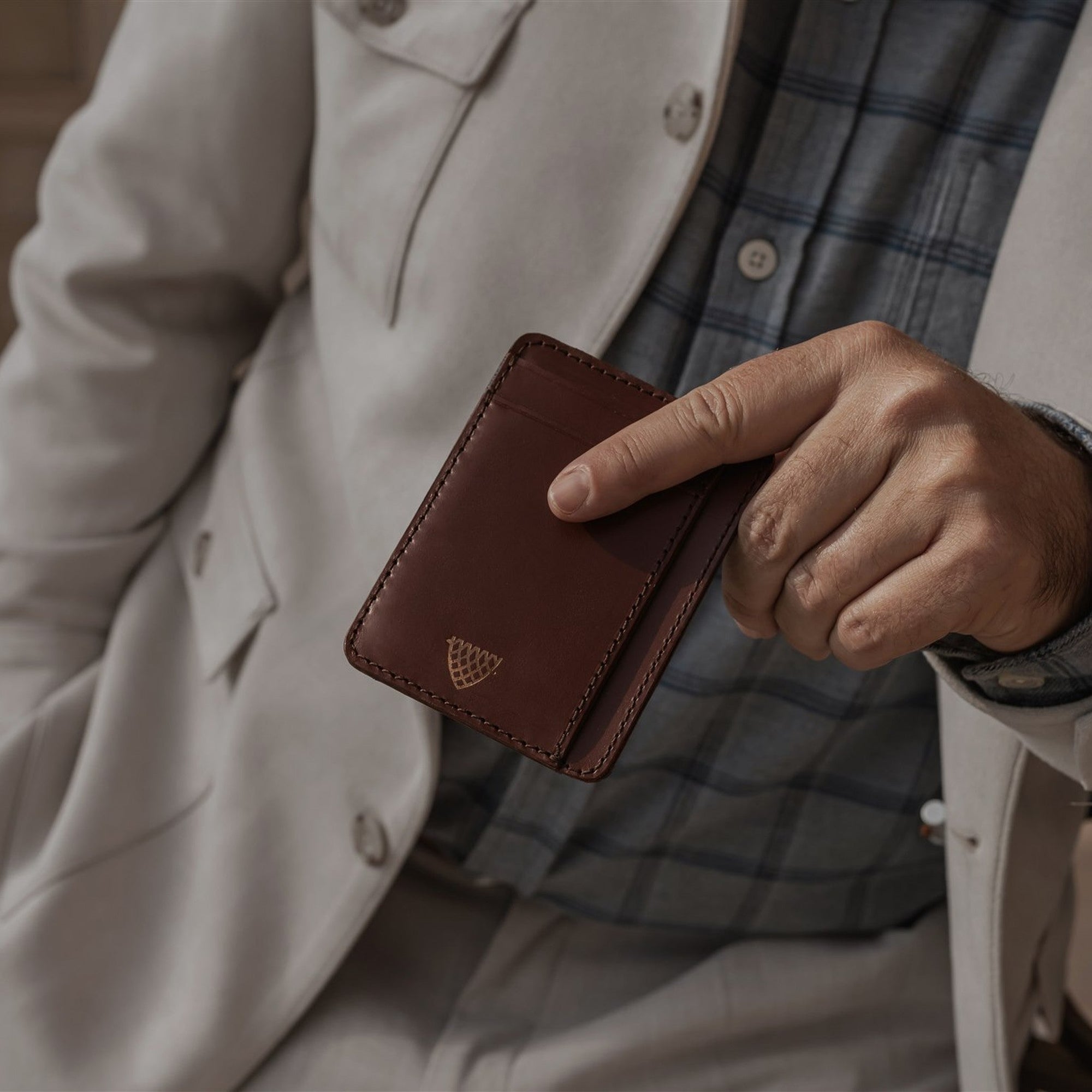 Man in a cream linen jacket holding the Jefferson Leather Slim ID Wallet in Elderwood Brown.